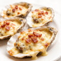 Baked oysters topped with melted cheese and bacon on a white plate